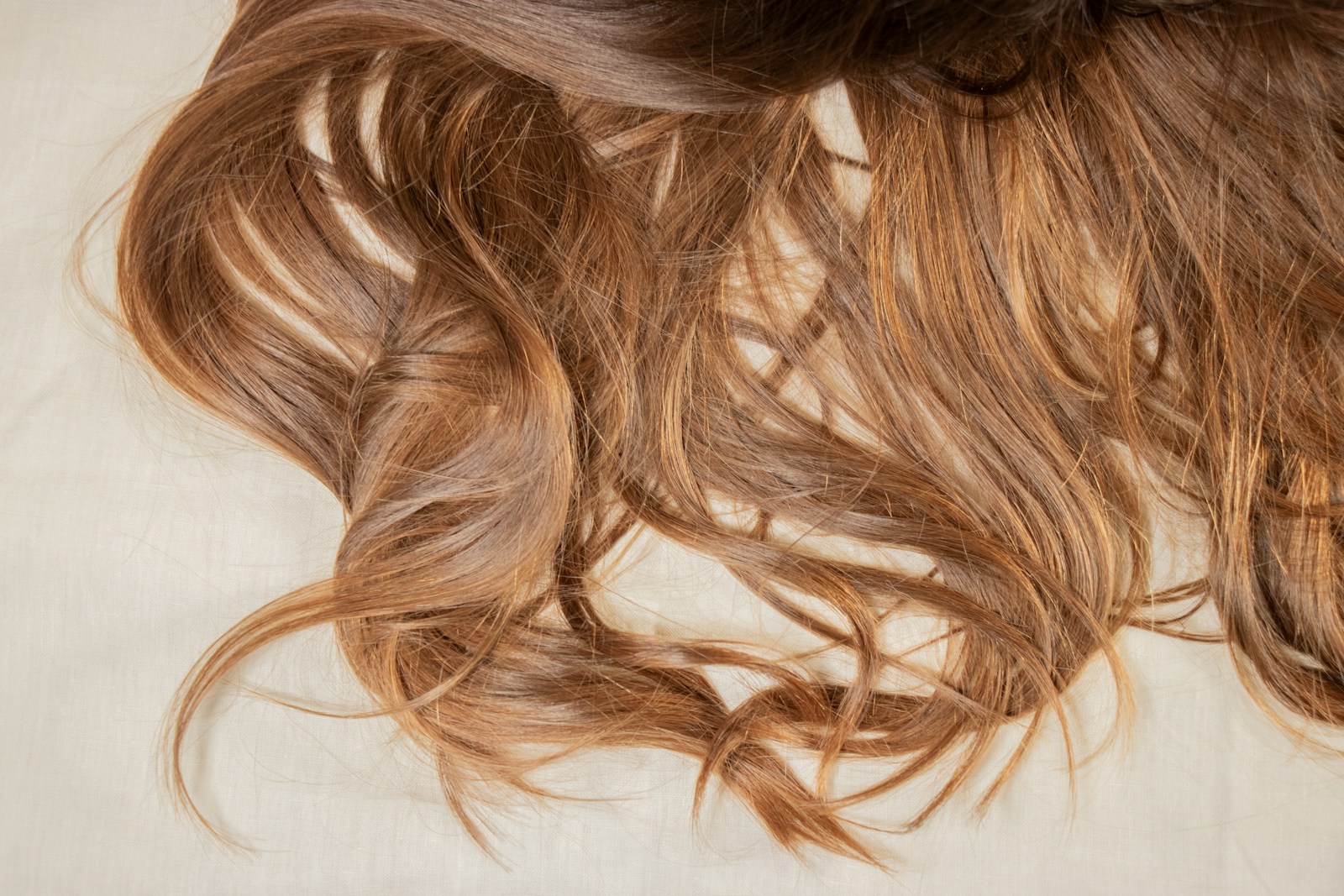 Loose strands of hair resting on soft, muted bedding, the quiet morning scene most mums first notice at around month 3 postpartum.