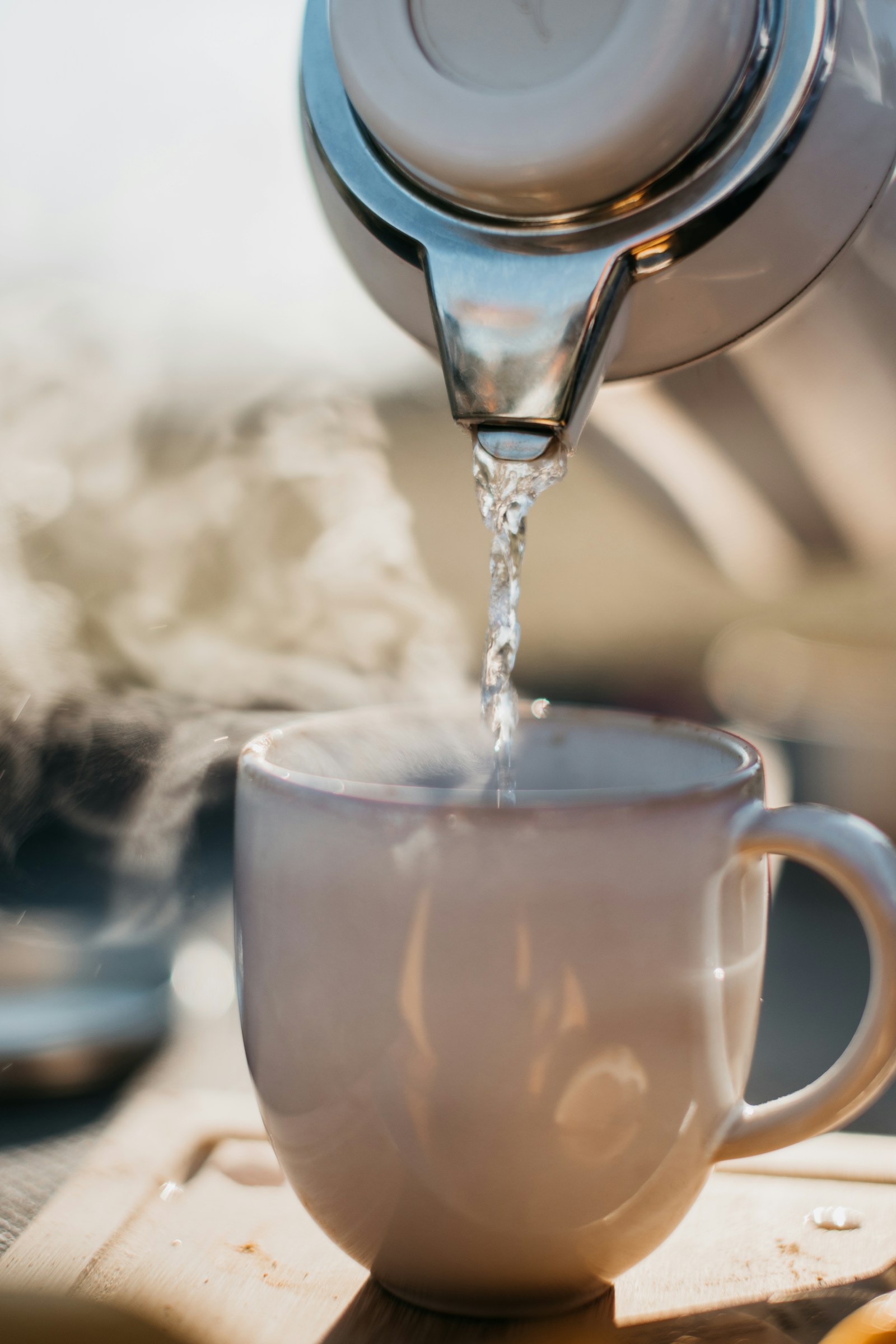 A kettle pouring clear hot water into a ceramic mug, soft steam catching the sunlight, the warm cup that the confinement rule was actually pointing at