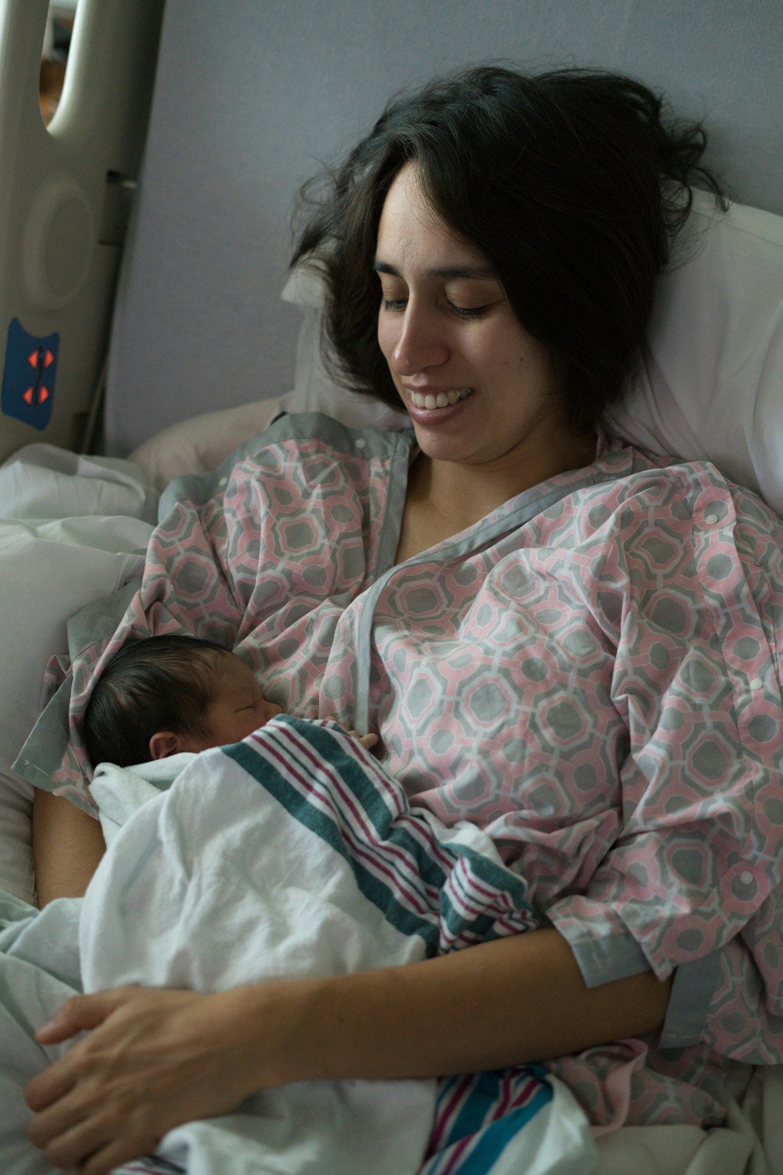 A new mother resting in a hospital bed cradling her newborn shortly after birth, the first stretch of C-section recovery