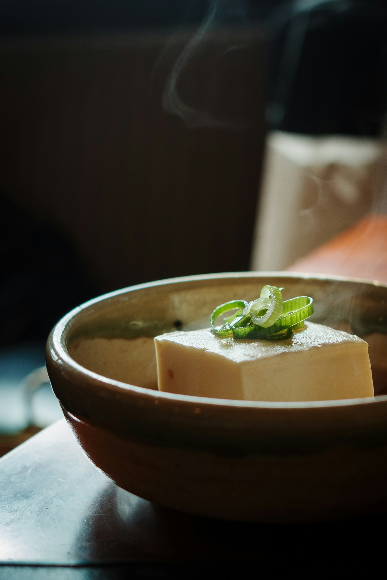 A steaming ceramic bowl of vegetarian confinement soup with soft tofu and chopped green onions, warm and gently plated, the kind of small hot dish a vegetarian mum gets three or four times a day during 月子.
